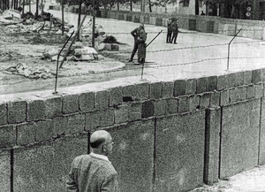 A West Berlin civilian stands alongside the newly erected Berlin Wall as East German border guards patrol the other side, August 1961. (Wikimedia Commons)